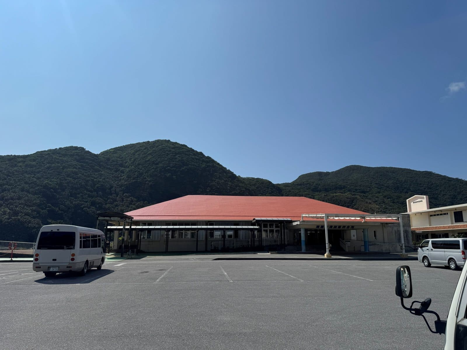 渡嘉敷港的紅屋頂港口建築與停車場,後方是島上的山