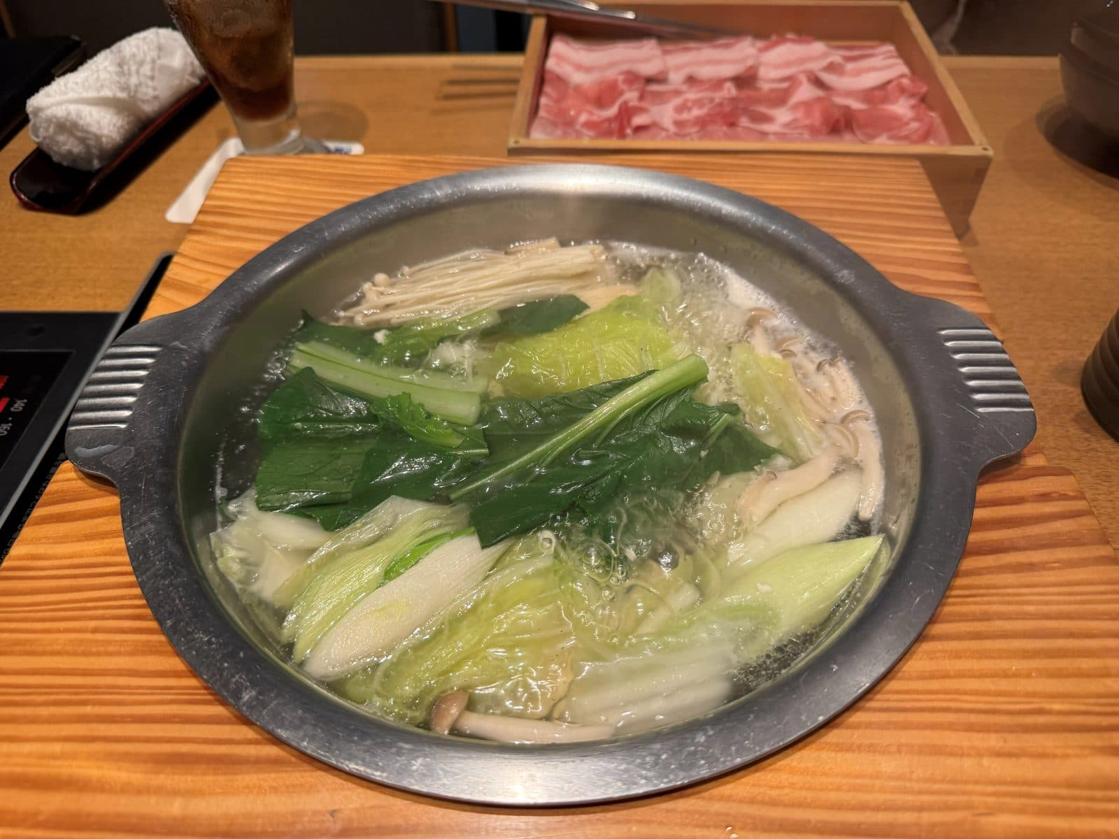鍋裡煮著白菜、青菜與菇類,後面是木盒裝的阿古豬肉片