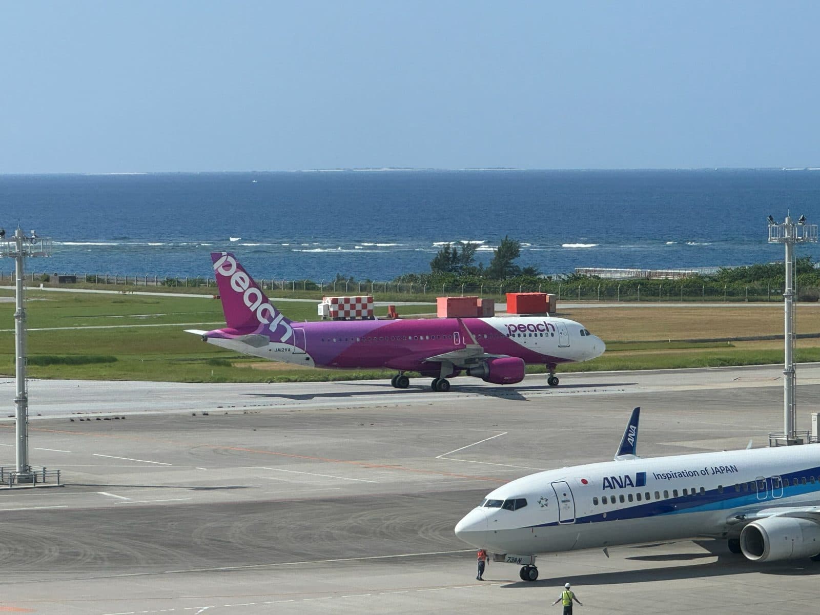 那霸機場停機坪上的 Peach 樂桃航空客機,後方是海